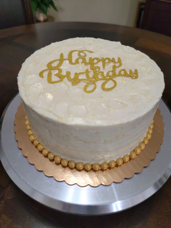 A white cake with gold lettering on top of it.
